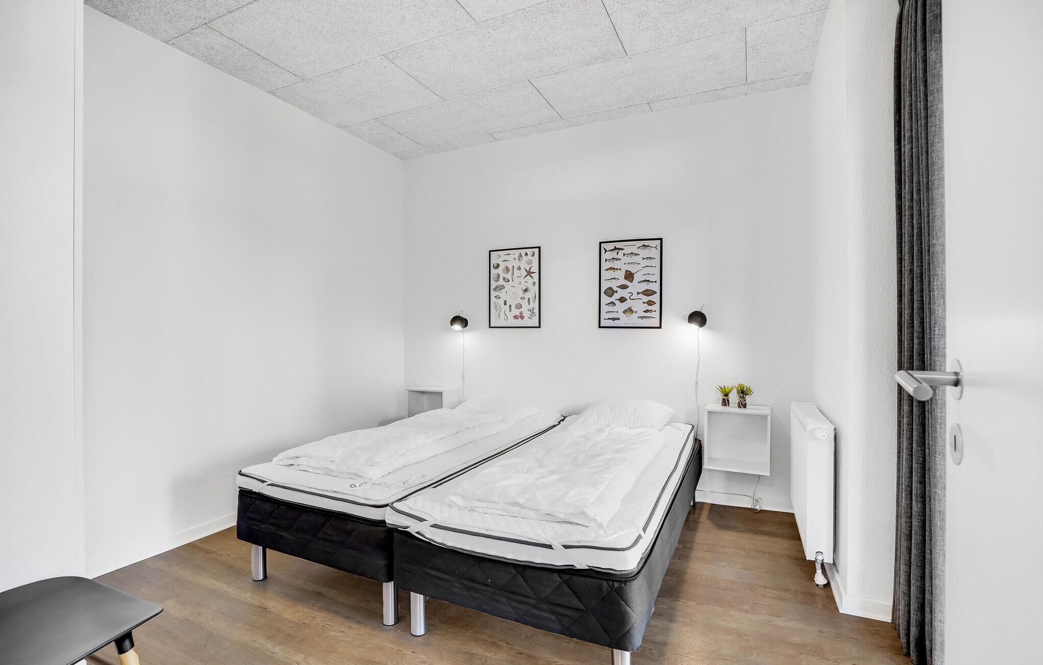 A minimalist bedroom with a double bed, two wall-mounted lamps, and a small bedside table with a plant.
