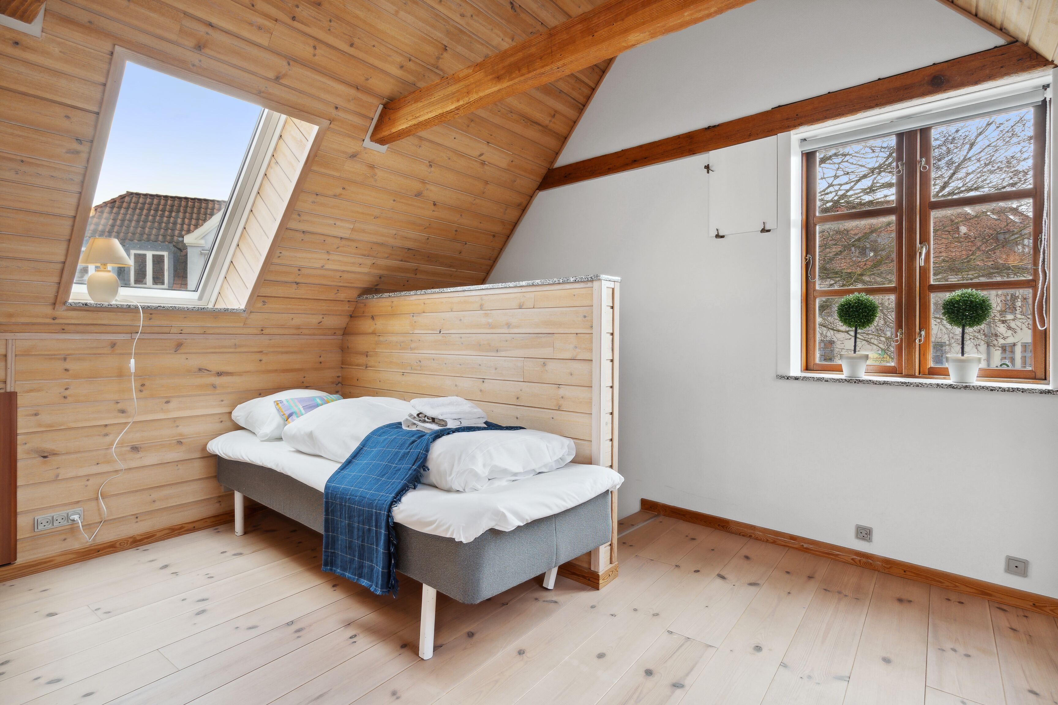 A bedroom with a sloped ceiling, a bed, a window with a view, and wooden walls.
