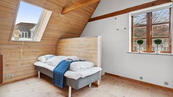 A bedroom with a sloped ceiling, a bed, a window with a view, and wooden walls.