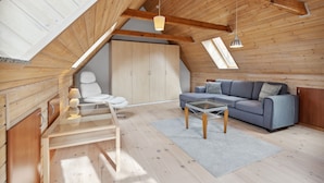 Un espacioso dormitorio tipo loft con techo inclinado, vigas de madera, un gran armario, un sofá, una mesa de centro de vidrio y una silla.