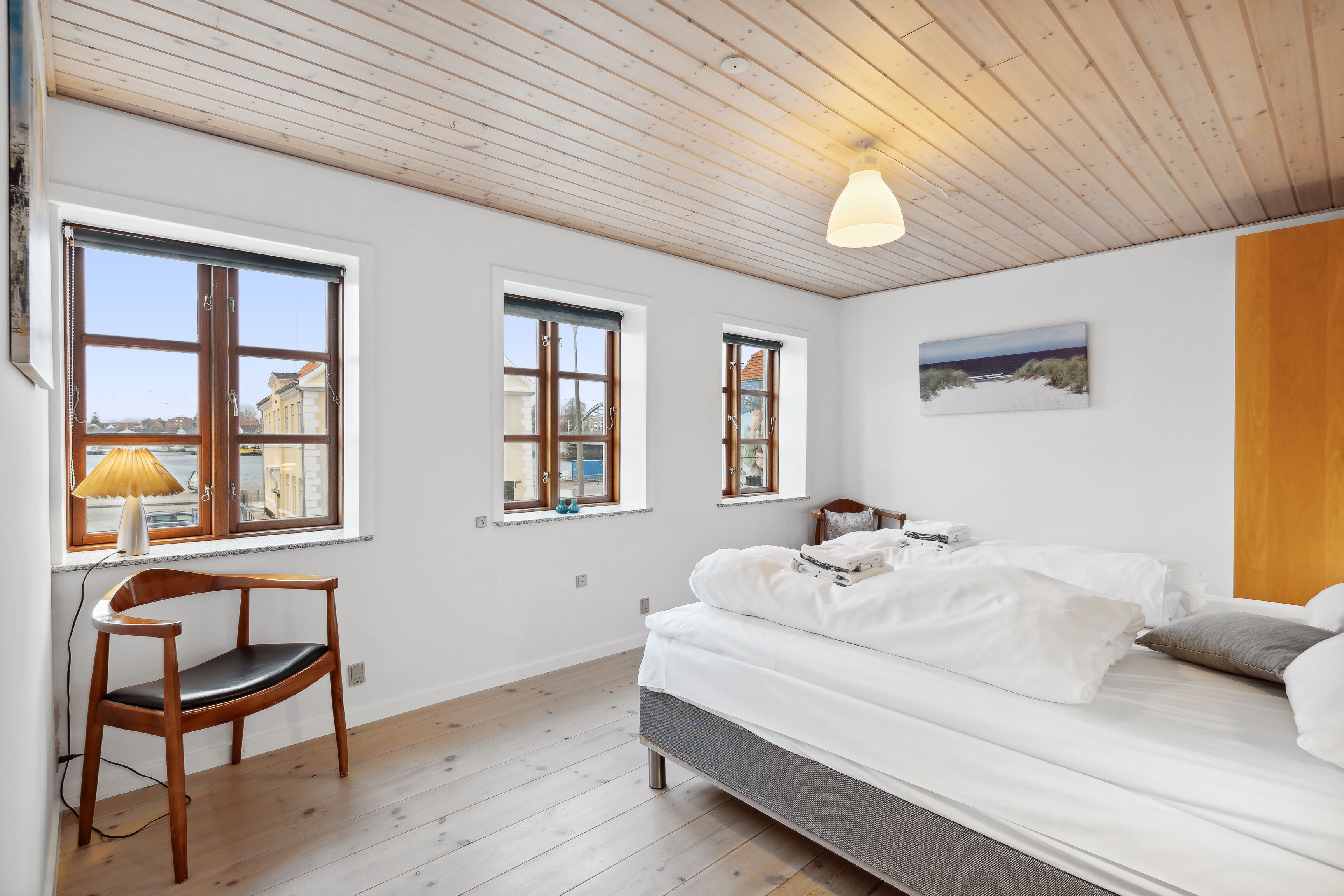 A bedroom with a bed, a wooden chair, and three windows.