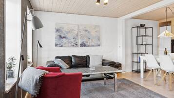 Una sala moderna con un sofá, una mesa de centro y un sillón rojo. Hay un cuadro en la pared y un comedor con una mesa y sillas.