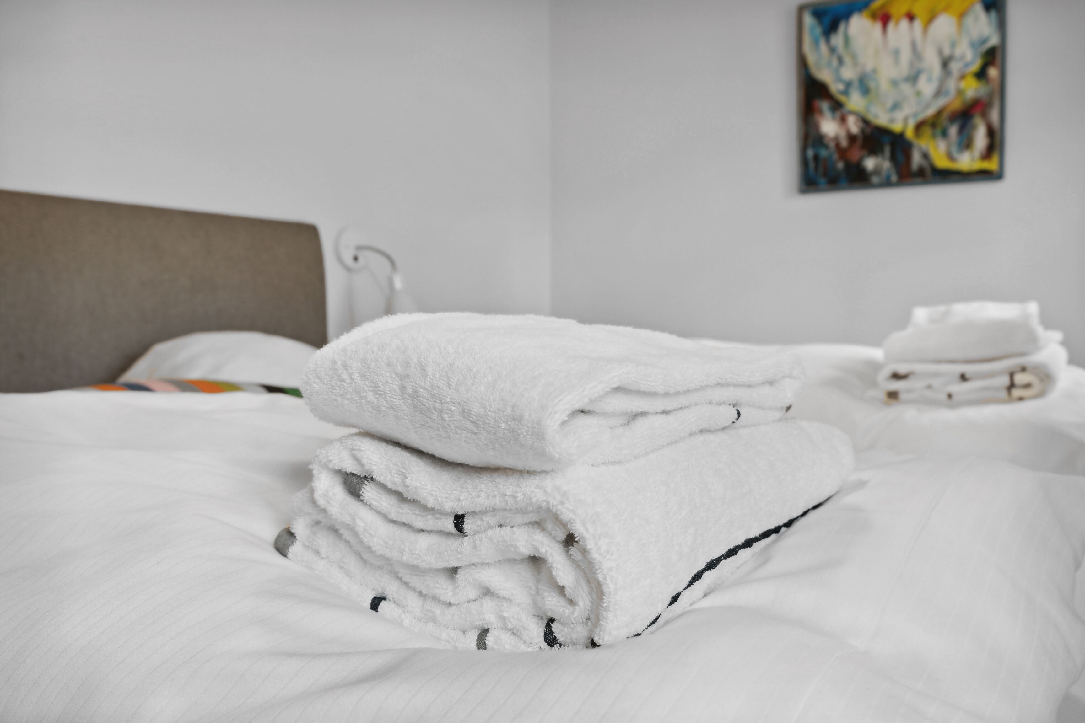 A neatly made bed with white linens and a folded towel on top.