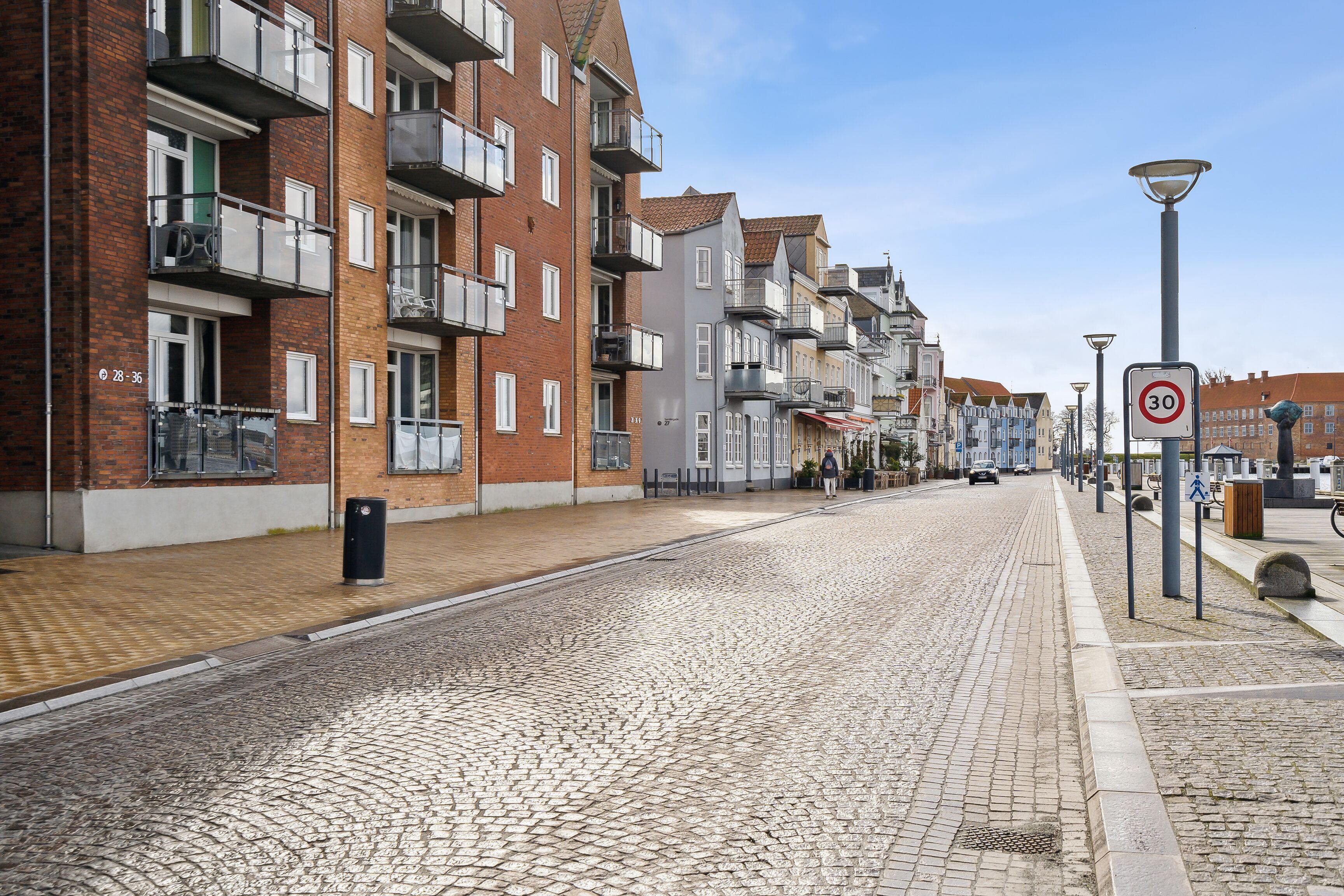 Una calle adoquinada flanqueada por edificios residenciales de varios pisos, una señal de límite de velocidad y un farol.
