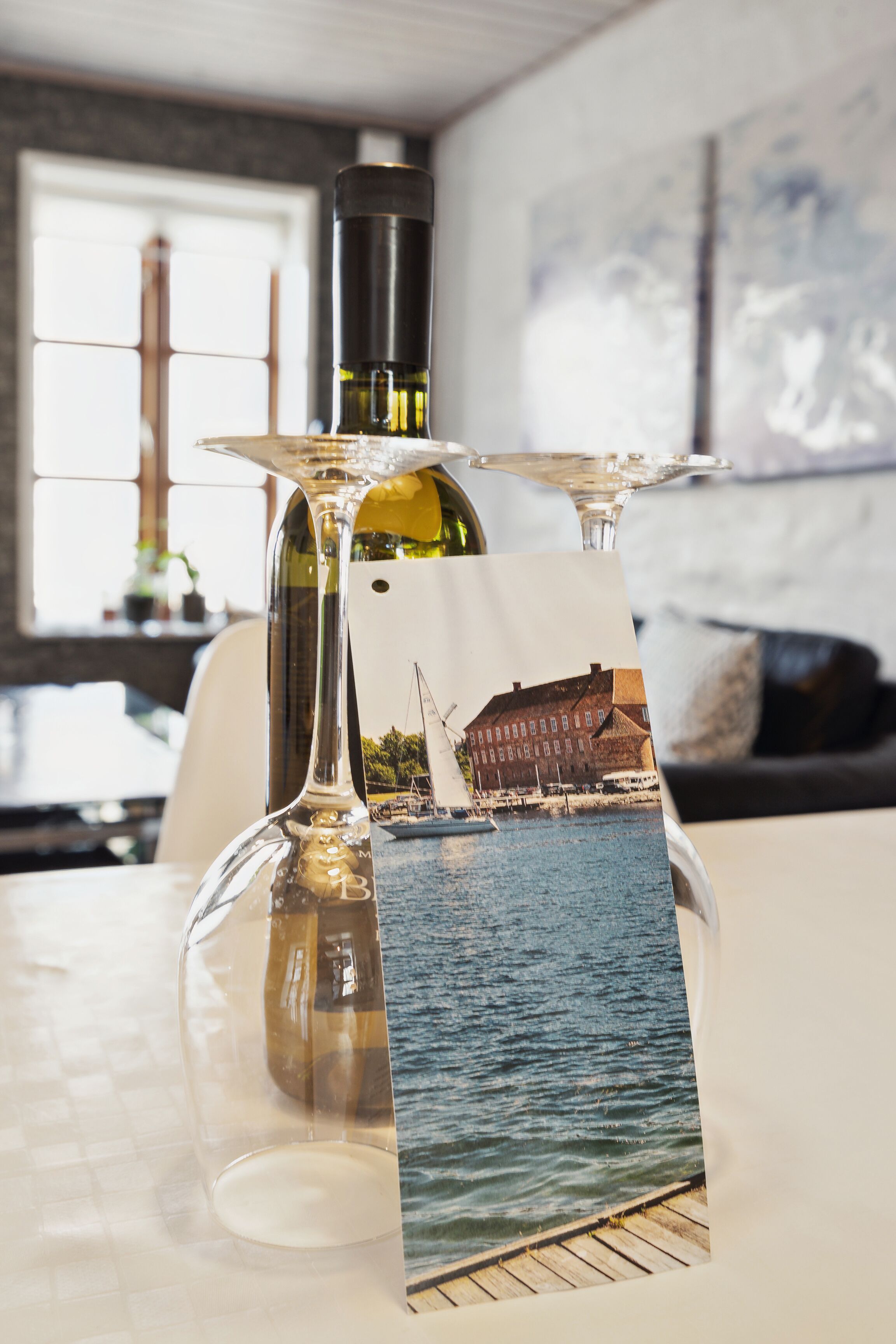 Ein Tisch mit einer Weinflasche, einem Glas und einer Postkarte mit einer Küstenansicht.