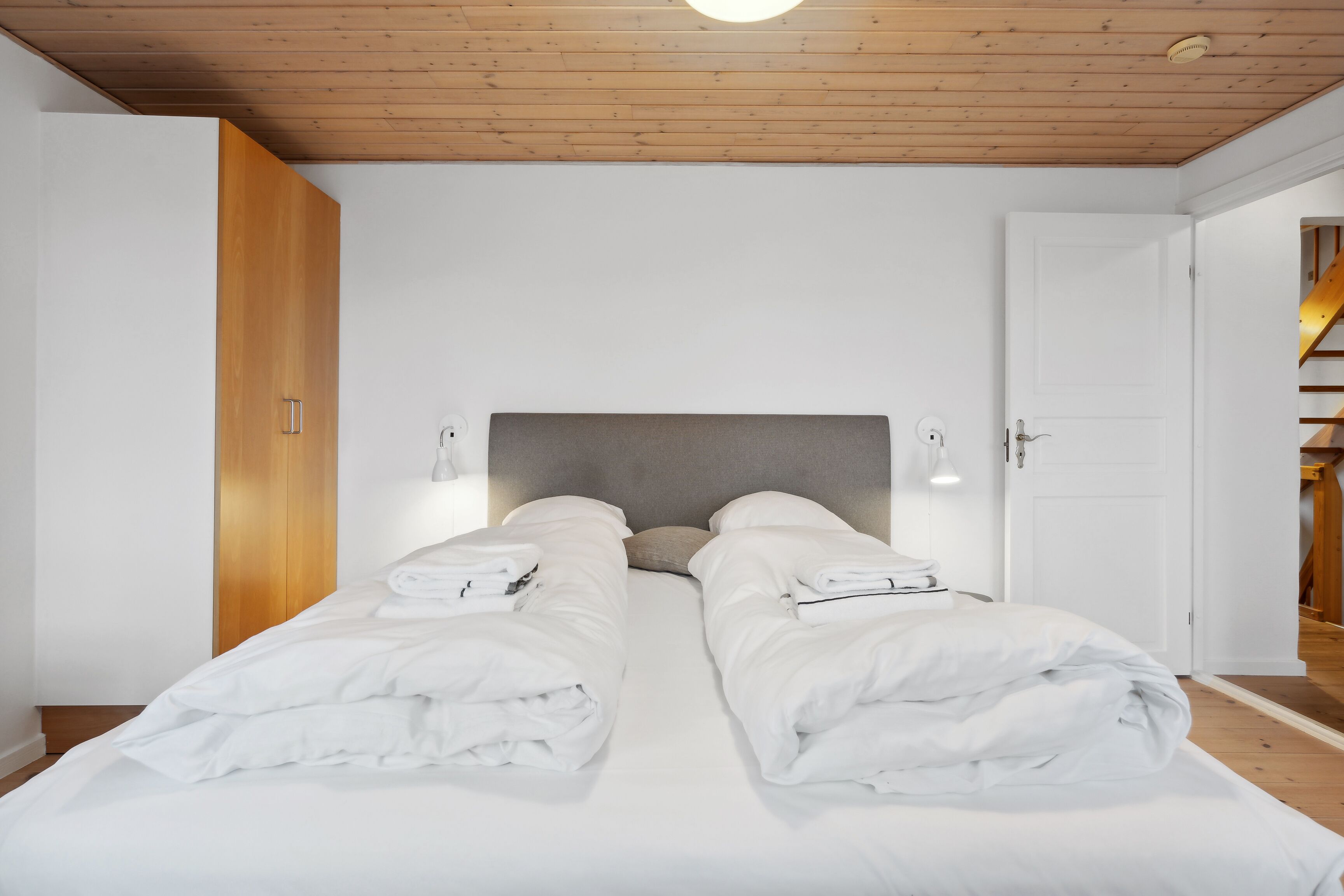 Un dormitorio con dos camas, techo de madera, paredes blancas y una puerta que da a otra habitación.