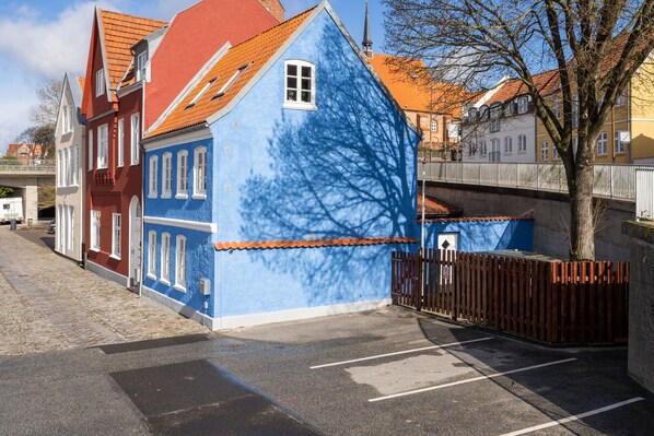 Vista callejera con un edificio azul, un edificio rojo y un árbol en primer plano.