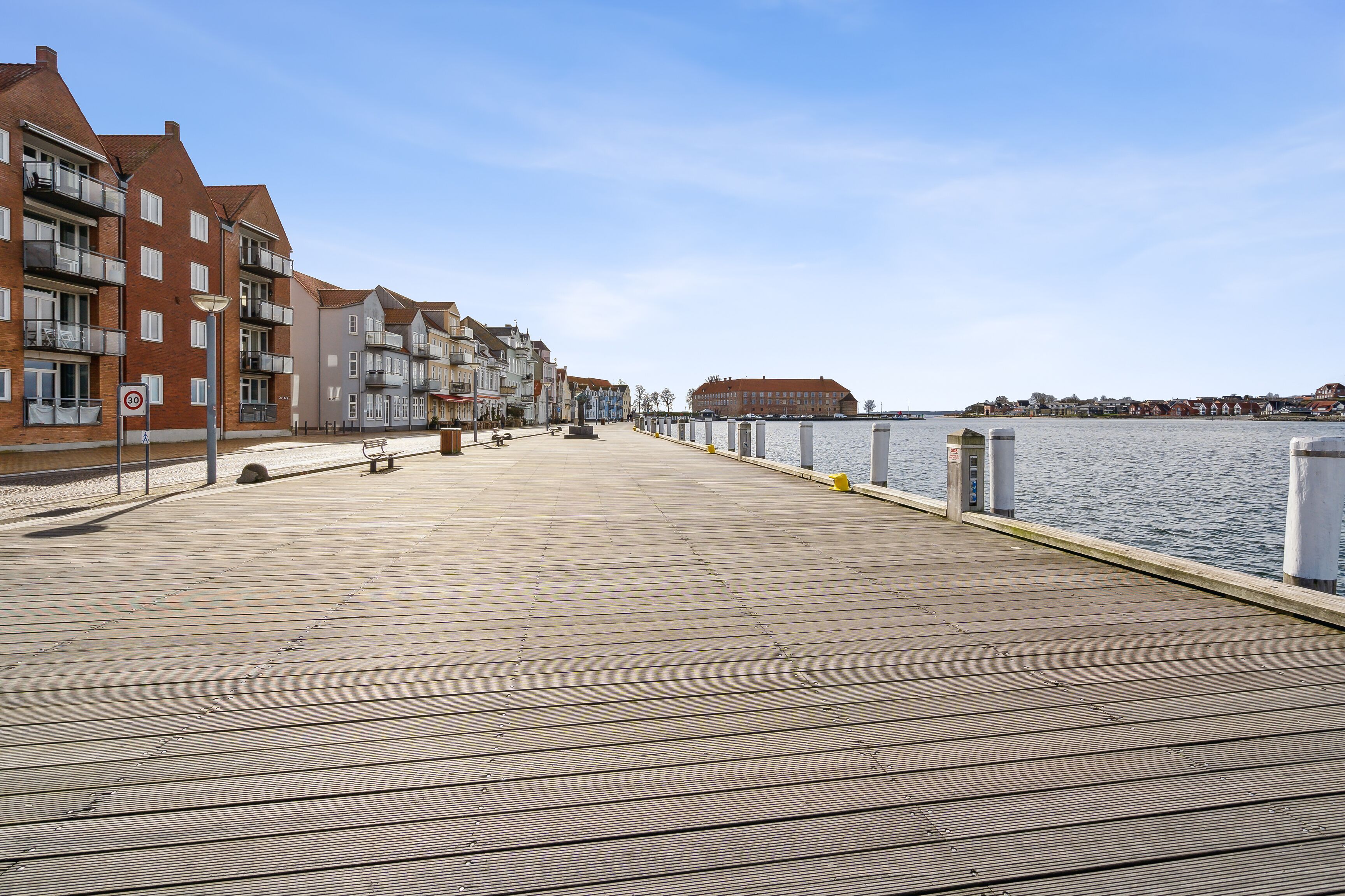 A wooden boardwalk with buildings on one side and a body of water on the other.