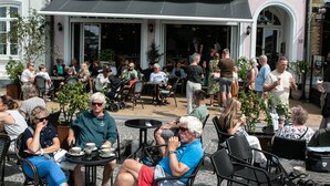 Un café al aire libre con mesas y sillas, rodeado por un edificio con un balcón.