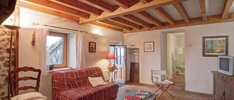 Une pièce chaleureuse avec un plafond en bois, un canapé rouge, une chaise en bois, une petite table avec des livres et un téléviseur posé sur un meuble.