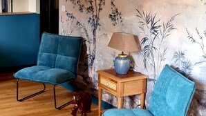A room with two blue chairs, a wooden side table with a lamp, and a wall mural. - La Pichonnière (Isigny-le-Buat)