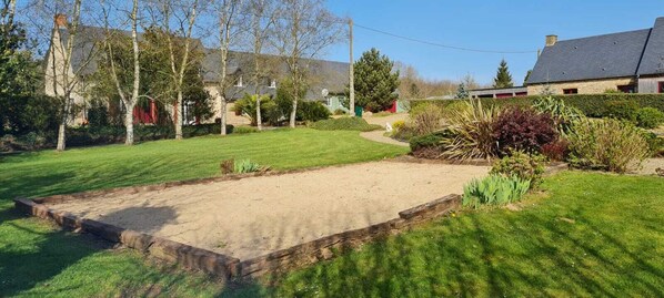 Un jardín cuidado con un arenero, rodeado de diversas plantas y árboles.