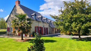A stone building with red shutters, a sloped roof, and a well-maintained lawn. - La Pichonnière (Isigny-le-Buat)