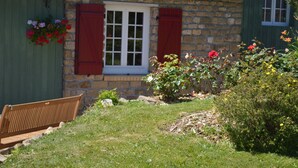 A stone building with a green exterior, a wooden bench, and a flower bed with red and yellow flowers. - La Pichonnière (Isigny-le-Buat)
