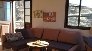 A cozy room with a wooden ceiling, a sofa, a small round table with a bottle, and a bulletin board on the wall. - Casa Monte for astro and nature lovers (Puntagorda)