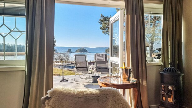 A cozy room with a view of a lake and mountains. It includes a table with chairs, a fireplace, and a window with curtains. - Amazing home in Vänersnäs with WiFi (Vänersnäs)