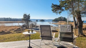 A deck with two chairs and a small table, overlooking a lake with trees and a distant shoreline. - Amazing home in Vänersnäs with WiFi (Vänersnäs)