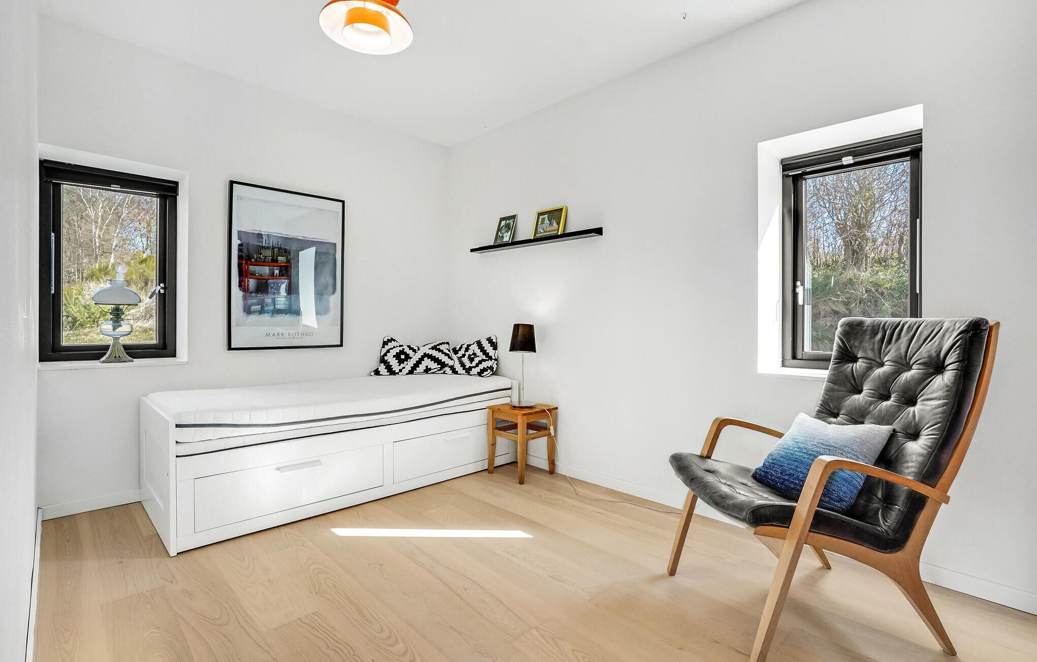 A modern room with a white sofa, a black leather chair, a wooden side table, and a picture frame on the wall.