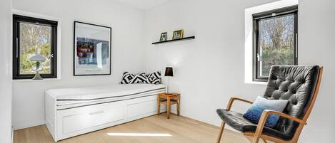 A modern room with a white sofa, a black leather chair, a wooden side table, and a picture frame on the wall.