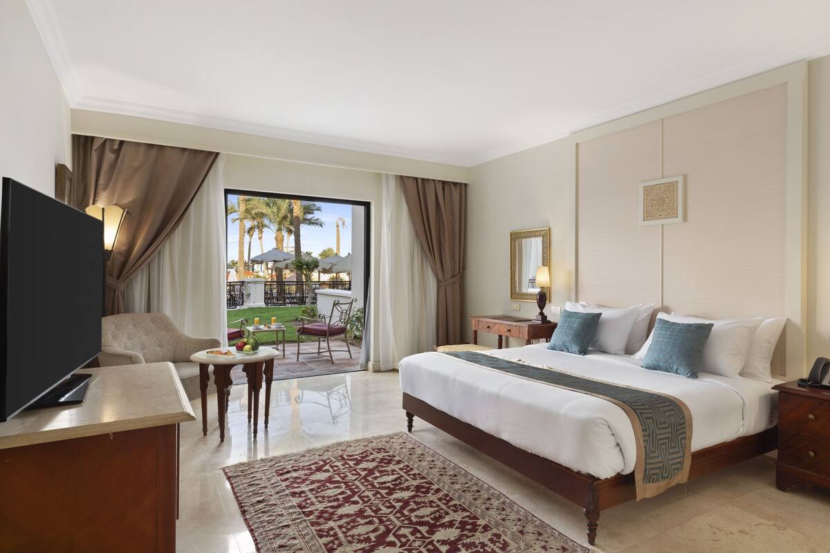 A hotel room with a large bed, a TV, a desk, and a view of the outdoor area.