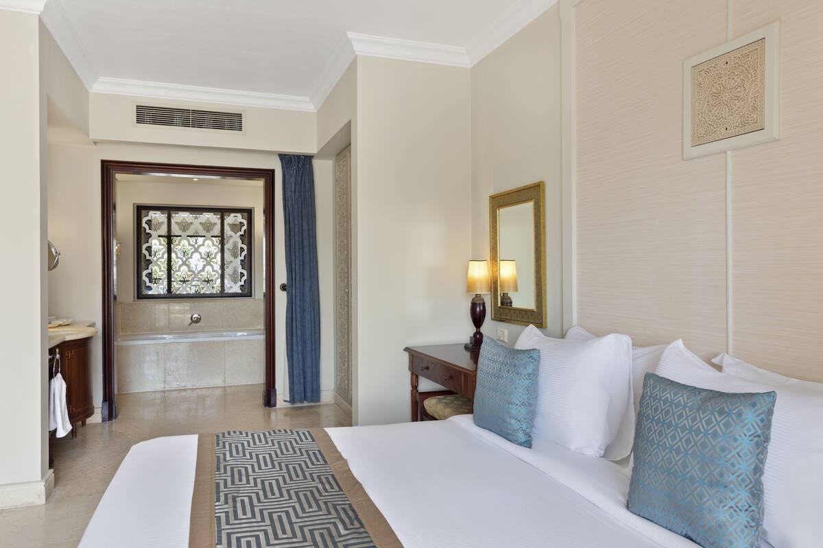 A hotel room with a large bed, a bathroom with a bathtub, a desk, and a mirror.
