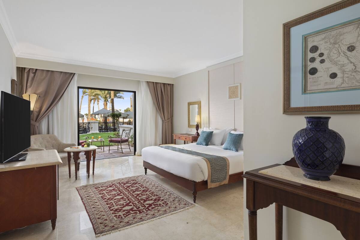 A hotel room with a bed, a desk, a TV, a large vase, and a view of the outdoors.