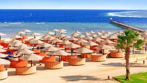 A beach with numerous thatched umbrellas and wooden cabanas, a pier extending into the ocean, and a clear blue sky. - Pickalbatros The Palace Port Ghalib (El Quseir)