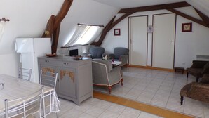 Een compacte kamer onder de dakrand met een kitchenette, een eethoek en een zithoek met een bank en stoelen.
