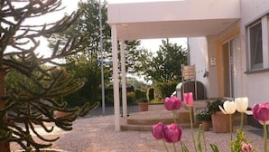 A garden with a patio area, a pergola, and a variety of plants including a large tree and tulips. - Lounge 4 - stylish apartment 51sqm, fully equipped, air conditioning, parking at the house (Koblenz)