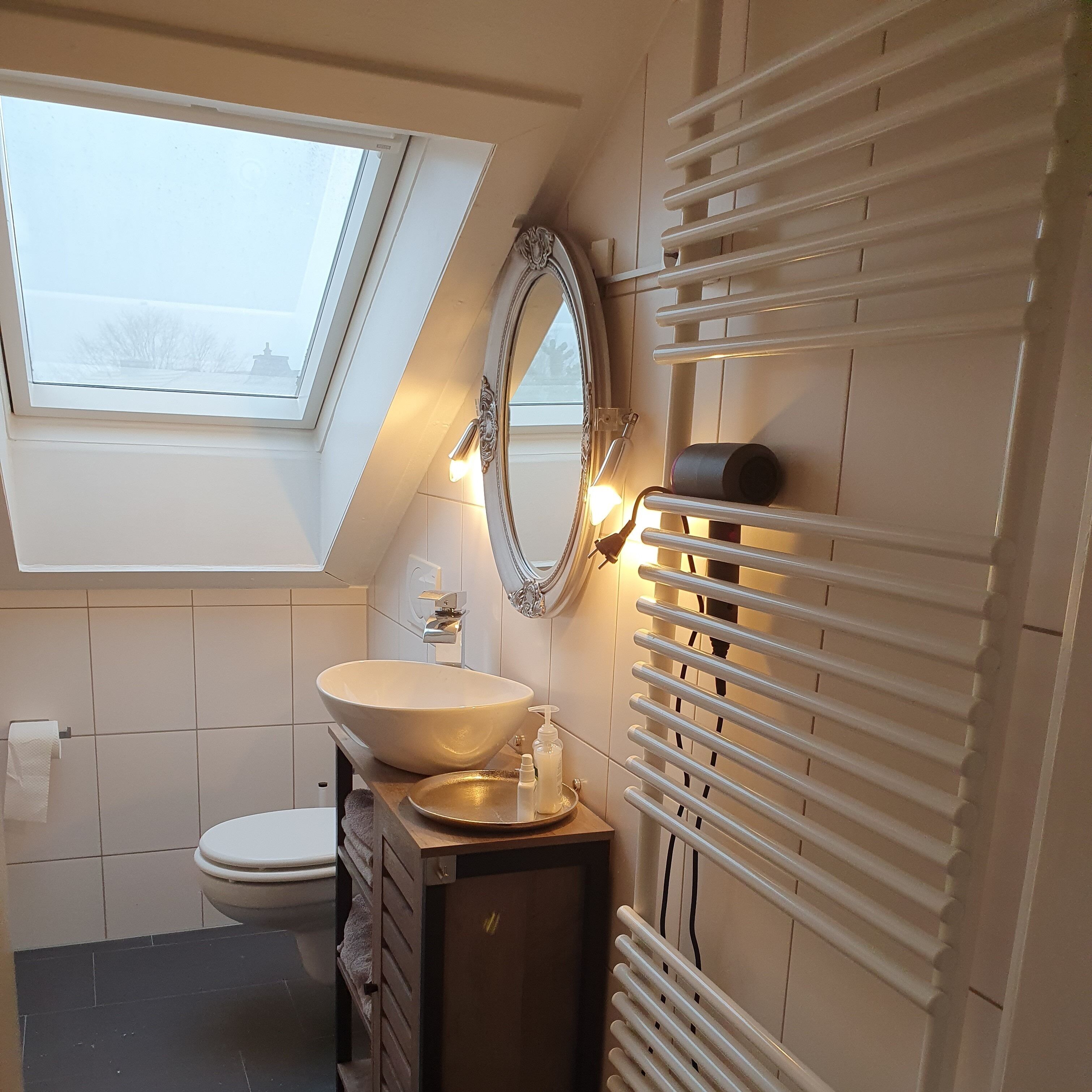 A bathroom with a skylight, a large mirror, a sink, and a radiator.