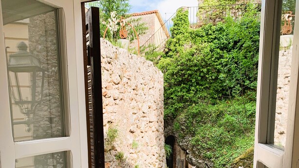 A view through an open window of a stone wall, a cobblestone path, and greenery. - Romantic cottage in the historic center of Collepardo (Collepardo)