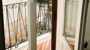 A view from a balcony with a metal railing, a white door, and a view of a street with buildings and greenery. - Romantic cottage in the historic center of Collepardo (Collepardo)