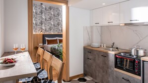 Een moderne keuken met een inbouwoven, een eethoek met tafel en stoelen, en uitzicht op een slaapkamer door een geopende deur.