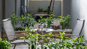 Een terras buiten met metalen stoelen, een ronde tafel en potplanten.