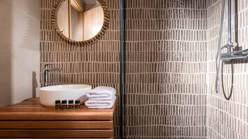 A bathroom with a wooden vanity, a white sink, a mirror, and a shower with a tiled wall.