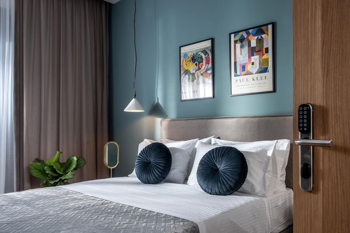 Een moderne hotelkamer met een bed, een plant, kunst aan de muur en een deur met een codeer slot.