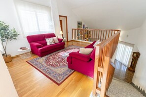 A living room with a red sofa, a patterned rug, wooden flooring, and a staircase with a wooden railing.