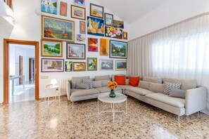 A living room with a large sectional sofa, a round coffee table, and a variety of framed artworks on the walls. - Fidalsa Paradise Pines (La Alcayna)