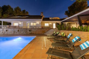 Una piscina con sillas de descanso y un muro de piedra.