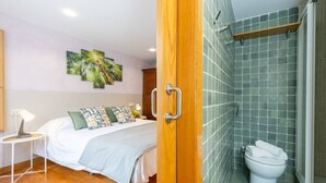 A hotel room with a bed, a bedside table with a lamp, a bathroom with a toilet and shower, and a wall with a green-tiled shower area. - Fidalsa Paradise Pines (La Alcayna)