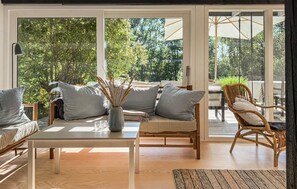 A cozy indoor seating area with a sofa, a chair, a table, and a view of the outdoors through large glass doors.