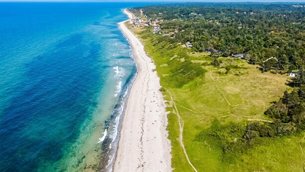 An aerial view of a coastal area with a beach, green fields, and scattered houses.