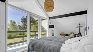 A bedroom with a large window, a bed with white bedding, a woven throw blanket, and a hanging light fixture.