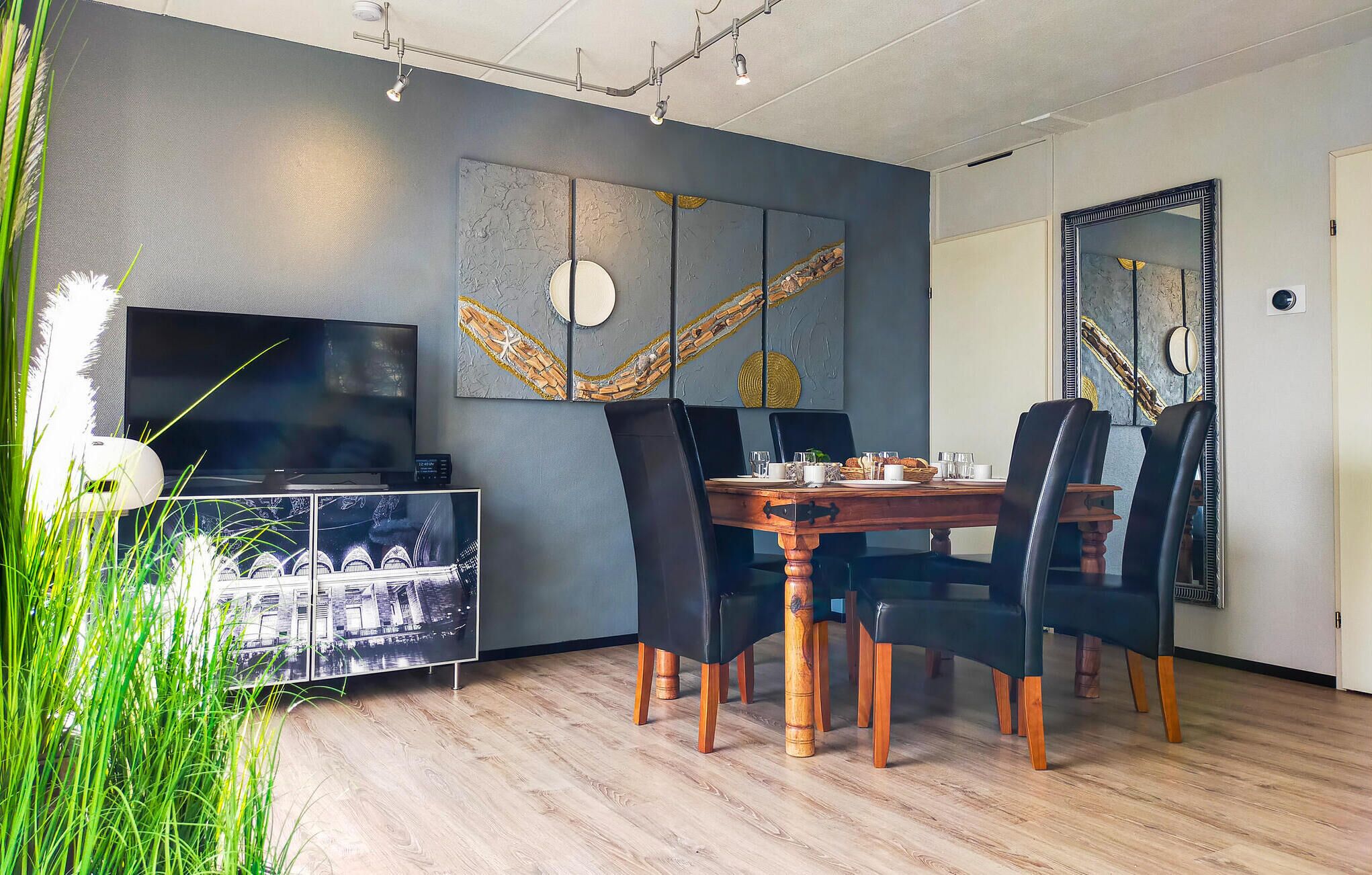 A dining area with a wooden table, black chairs, and a TV on a cabinet.
