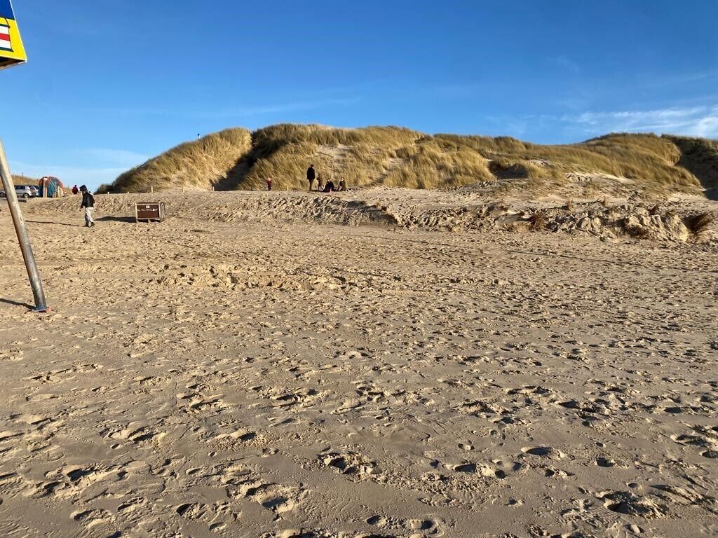Ein sandiger Strand mit Fußspuren und Dünen im Hintergrund.