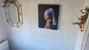 A room with a white brick wall, a framed painting, a geometric mirror, and a small round table.