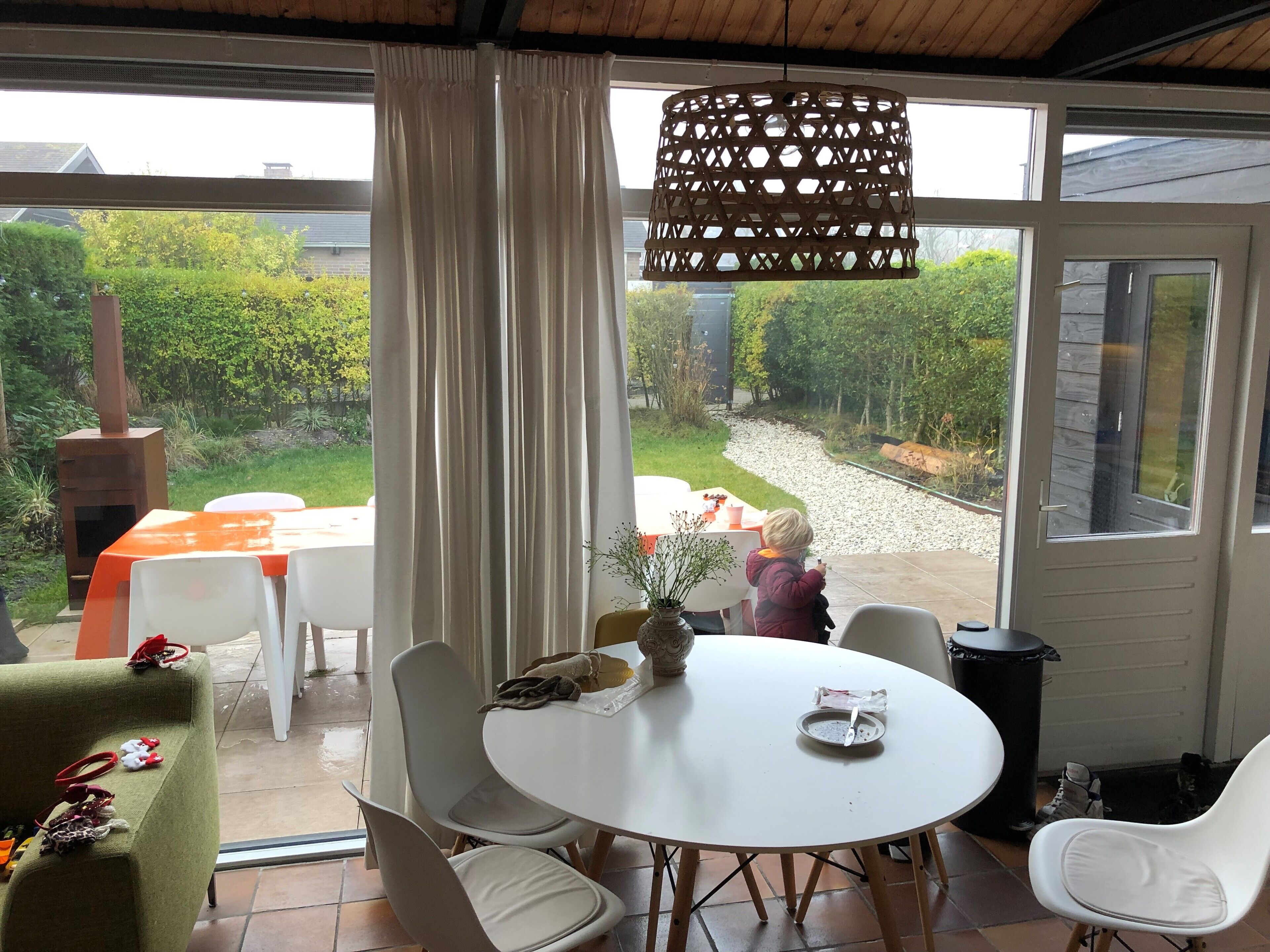 Uma sala de jantar com uma mesa redonda, cadeiras brancas e vista para um jardim através de grandes janelas.