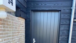 A dark wooden door with a metal handle and a small plate, a brick wall, and a concrete pavement.