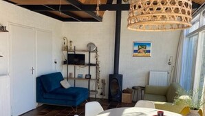A modern living room with a round dining table, white chairs, a blue sofa, and a wooden ceiling.