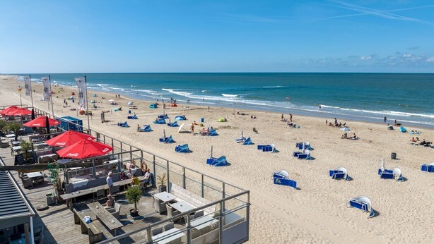A beach with umbrellas, sun loungers, and a wooden deck with tables and chairs.